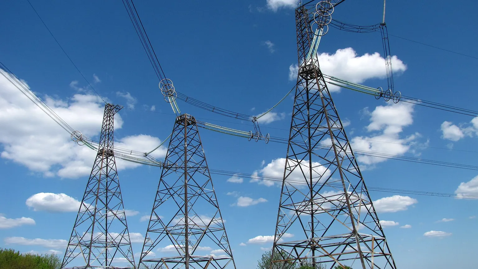 High-voltage pylons crossing a landscape toward a city skyline at dusk